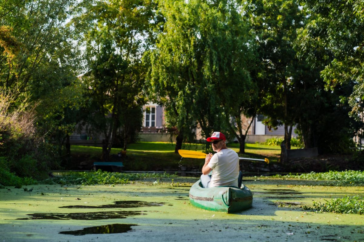 Homme dans un canoë sur un canal du Marais poitevin recouvert de lentilles d'eau